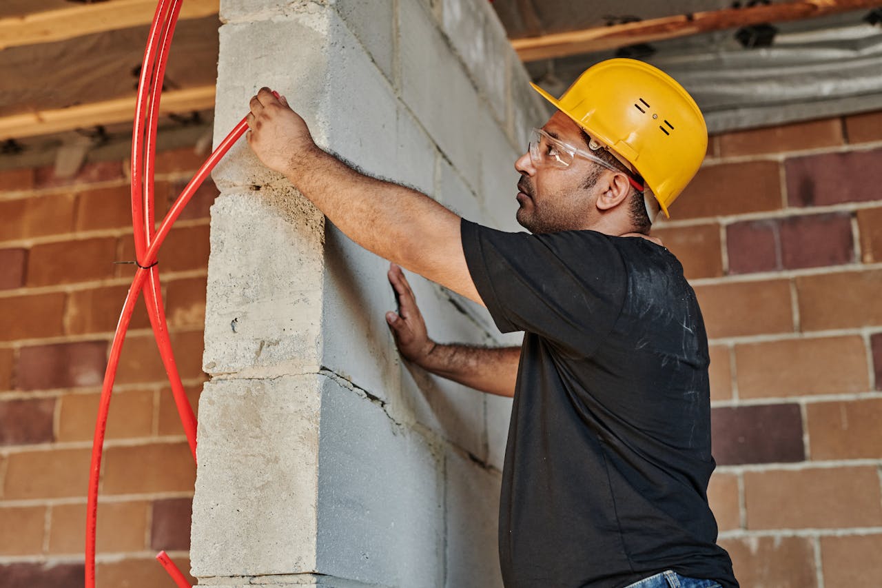 Construction worker with hard hat installing electrical cables on a site.